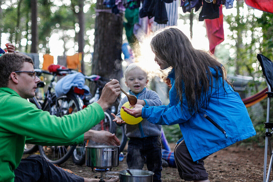 Familie auf dem Zeltplatz, Abendessen Vater gibt Kindern essen, kochen, Kocher, Mädschen (12 Jahre) und Junge (2 Jahre), trocknende Wäsche, Wald, Campingplatz, Radtour einer Familie, Sommer, Ostsee, MR (Vater und Sohn), Zeltplatz Regenbogencamp bei Bakenb