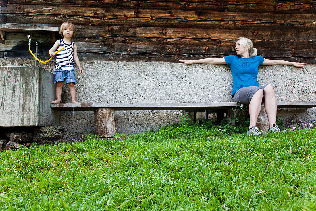 Woman and child on a bench infront of a farmhouse, Kloaschau Valley, Bayrischzell, Bavaria, Germany