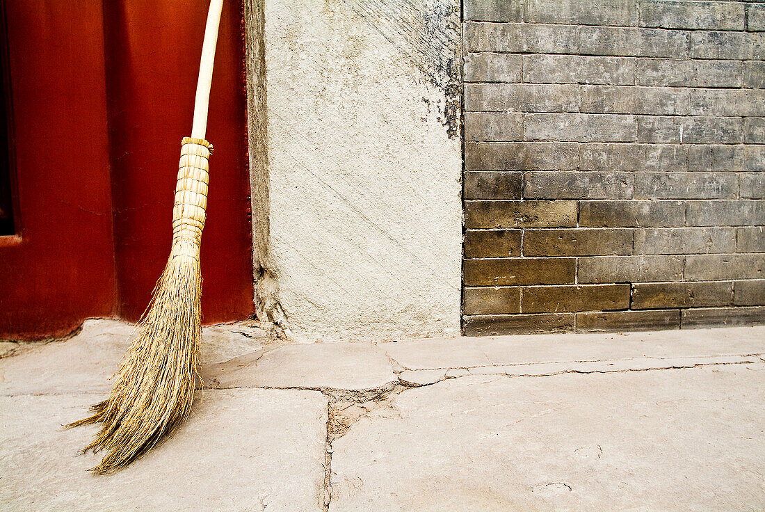 China, Beijing, A broom leaning against a cement wall, common street scene.