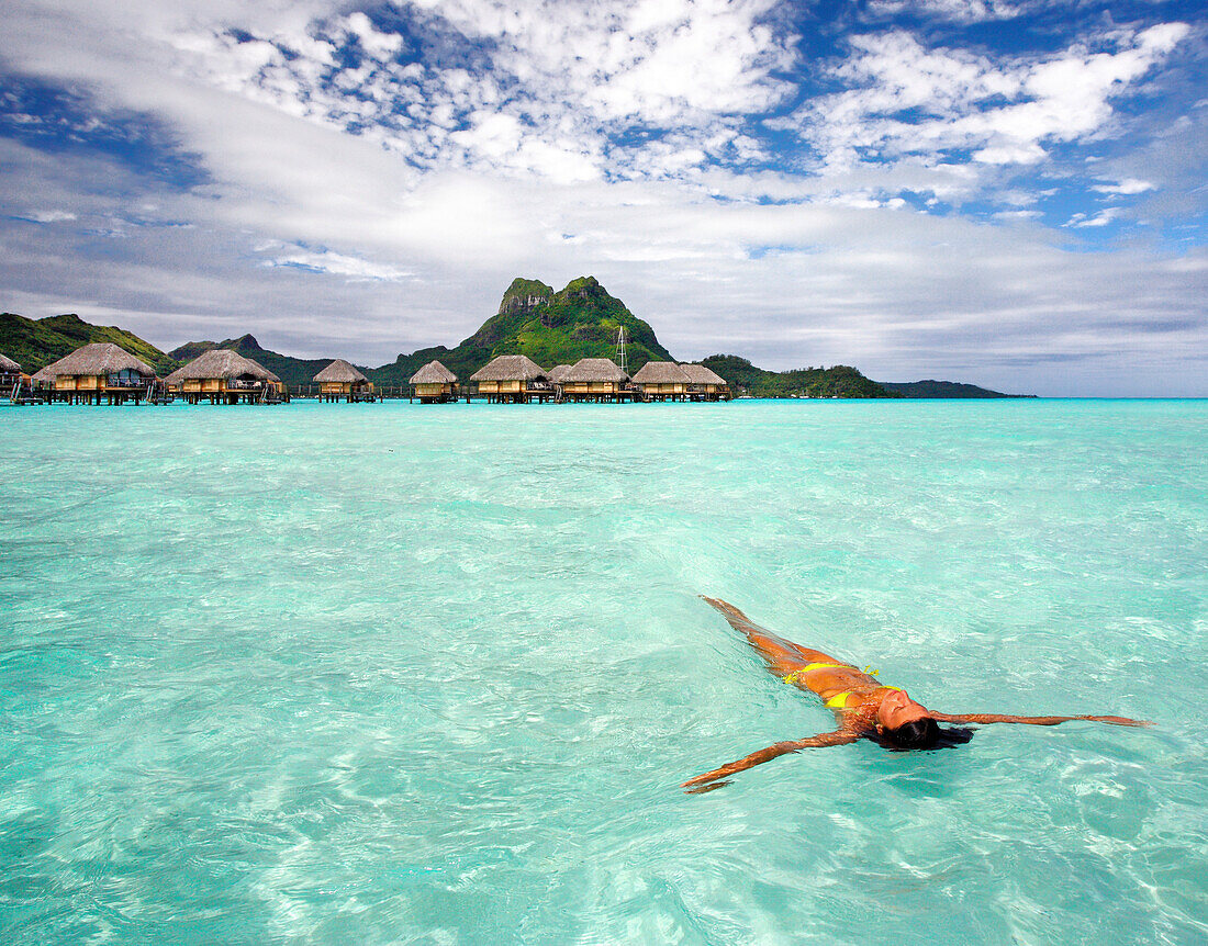 French Polynesia, Tahiti, Bora Bora, Woman floating in water near resort.