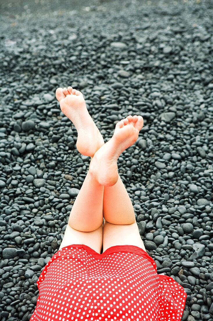 Girls legs, feet in air on black rocks.