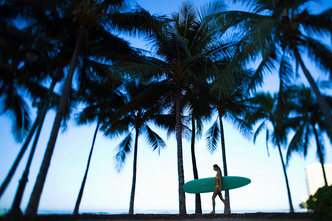 Hawaii, Oahu, Waikiki, Woman walking with surfboard.