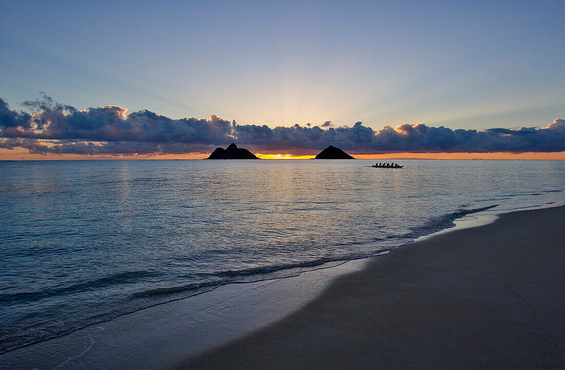 Hawaii, Oahu, Lanikai, sunrise with the Mokulua islands and outrigger canoe in the distance.