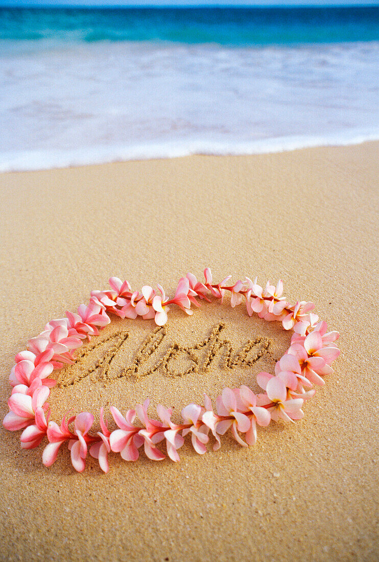 Hawaii, Turquoise ocean waters, foaming shore water, pink plumeria lei, ALOHA written in sand