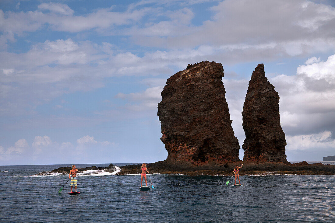 Hawaii, Lanai, Three young friends stand-up paddle boarding off the coast.