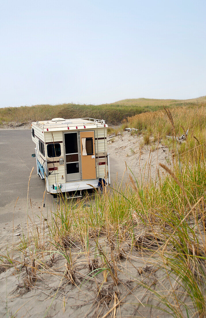 A motorhome or camper, an RV parked on a beach by sand dunes. Back door open. Fishing gear in the back of the vehicle., Cape Disappointment State Park, Washington, USA