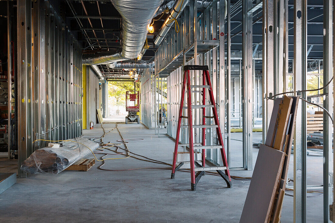 A commercial building under construction. View along the central corridor, with roof ducts and light gauge steel framing. A ladder., Seattle, Washington, USA. Commercial Construction Project