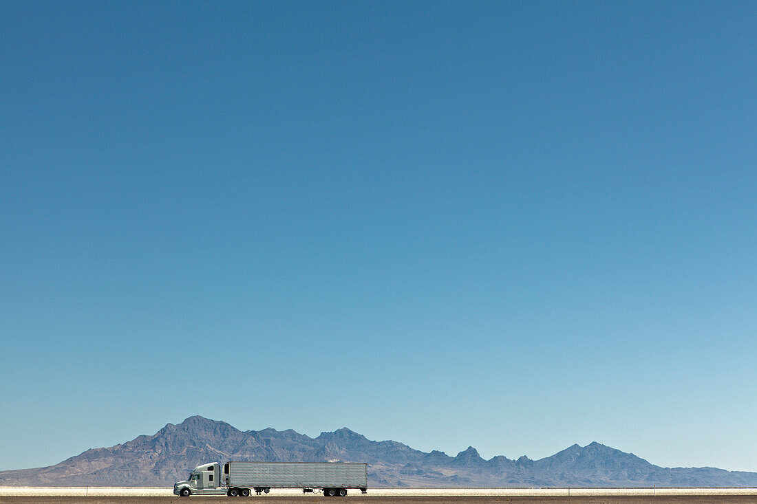A lone semi-trailer truck on an empty highway, Hwy. 80, at Bonneville Salt Flats, with distant mountain range and big clear blue sky., Bonneville Salt Flats, Utah