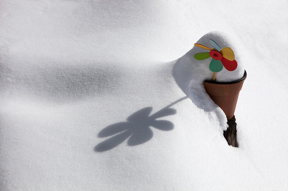 windmill toy in a clay pot in a private garden covered with snow