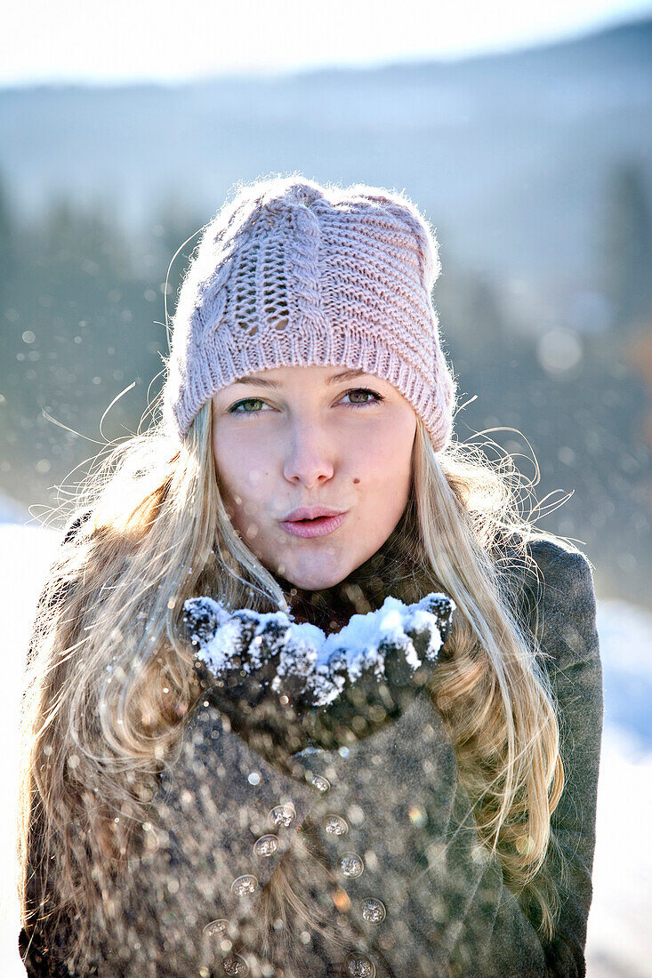 Junge Frau pustet Schnee aus den Händen, Steiermark, Österreich