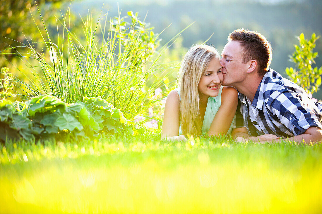 Young couple lying on grass, man kissing woman, Styria, Austria