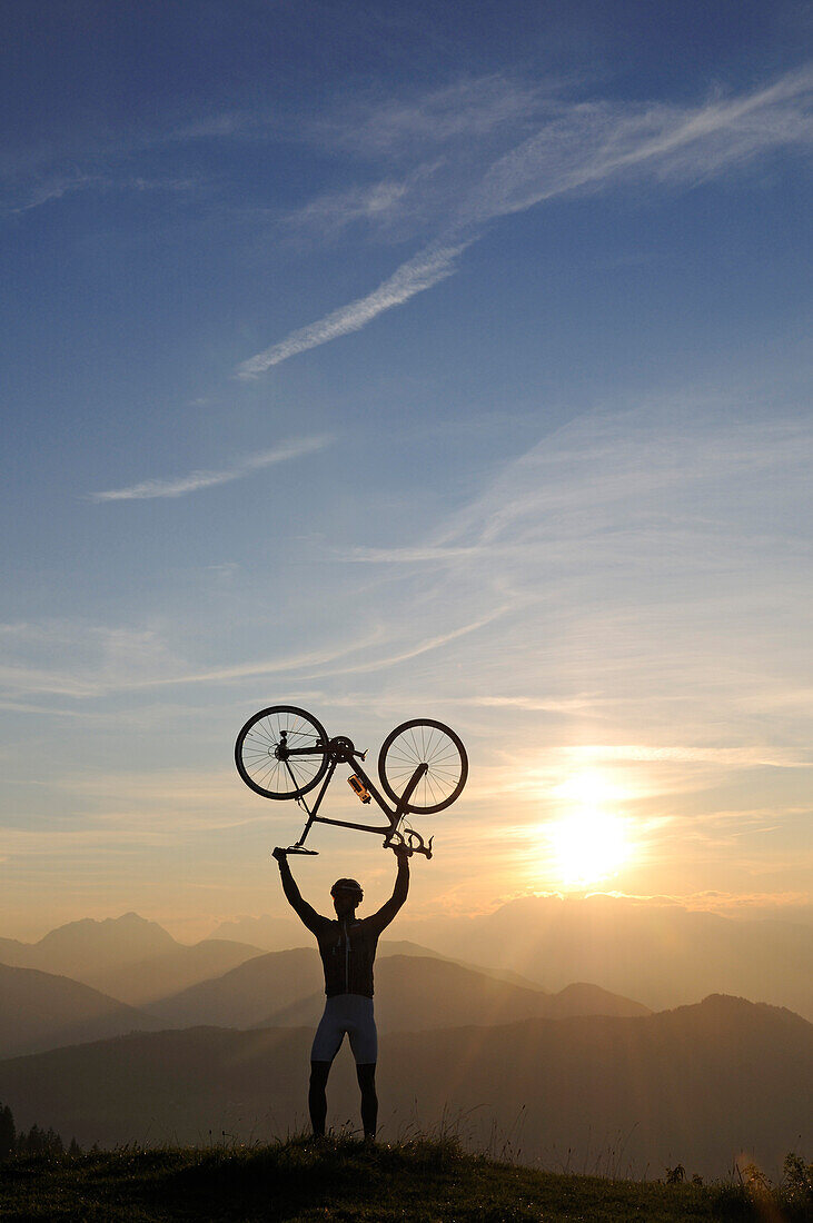 Man holding his racing bike over his head, Kraftalm, Hohe Salve, Kitzbuehel Alps, Tyrol, Austria