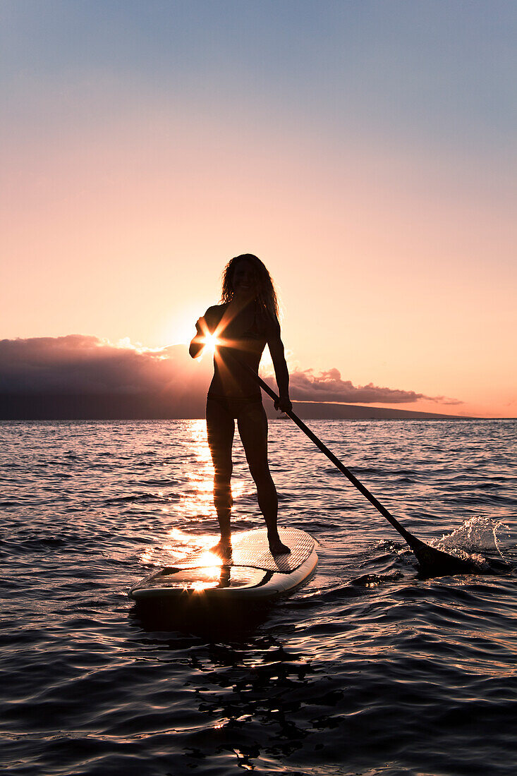Hawaii, Maui, Woman stand up paddling in ocean just off Canoe Beach, Silhouette at sunset.