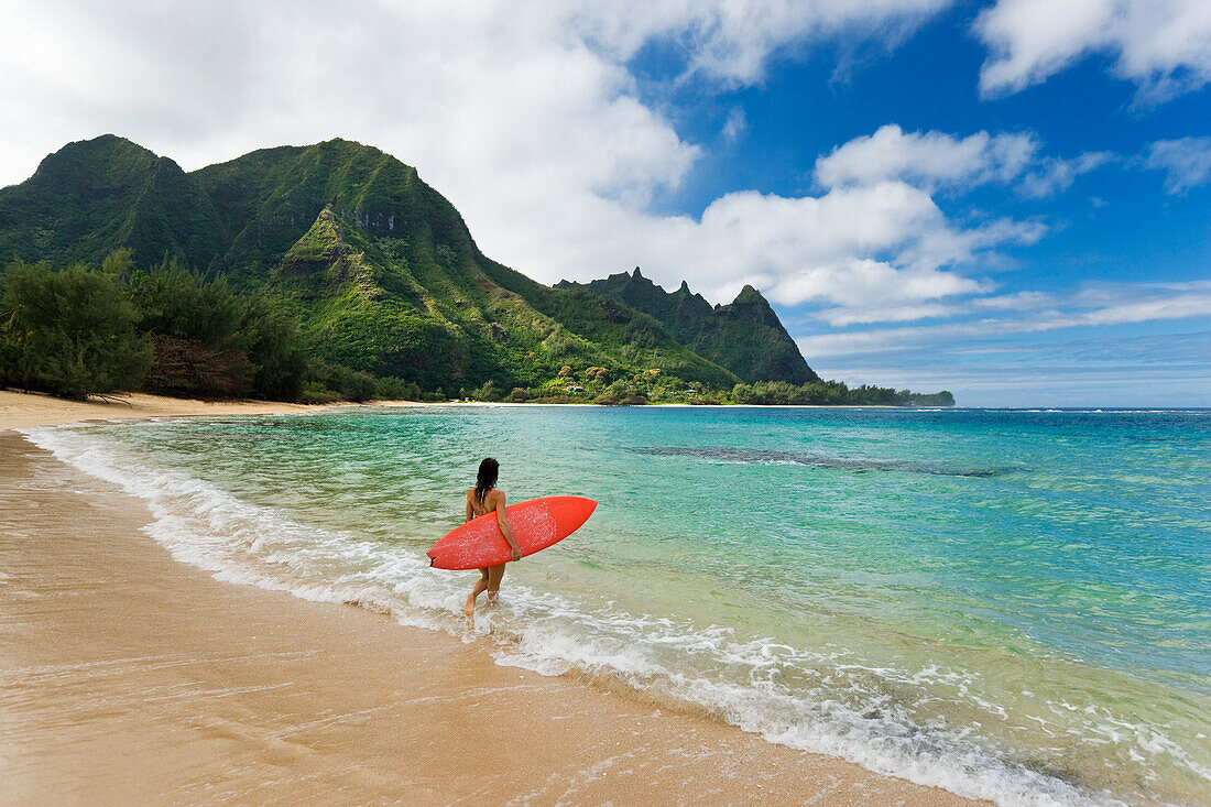 Hawaii, Kauai, Haena Beach Tunnels Beach, Woman entering ocean with surfboard.