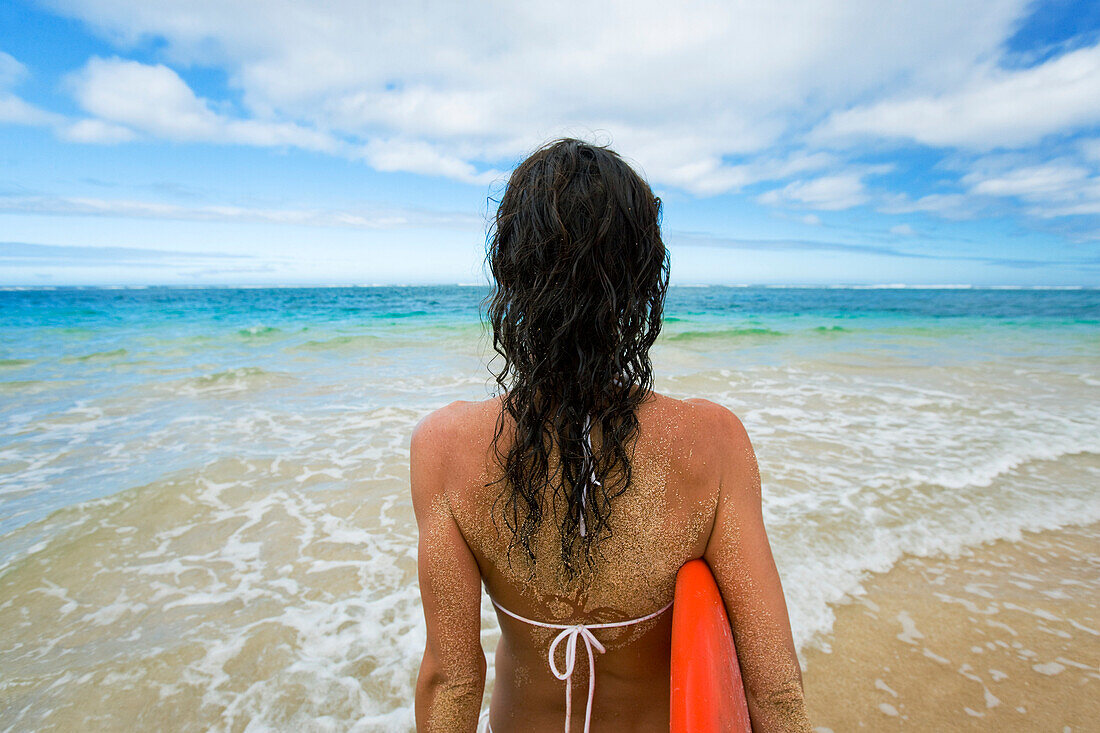 Hawaii, Kauai, Woman holding surfboard on beach, View from behind.