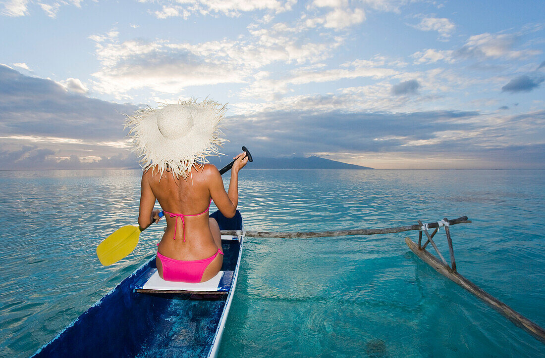 French Polynesia, Moorea, Woman paddling in ocean in outrigger canoe.