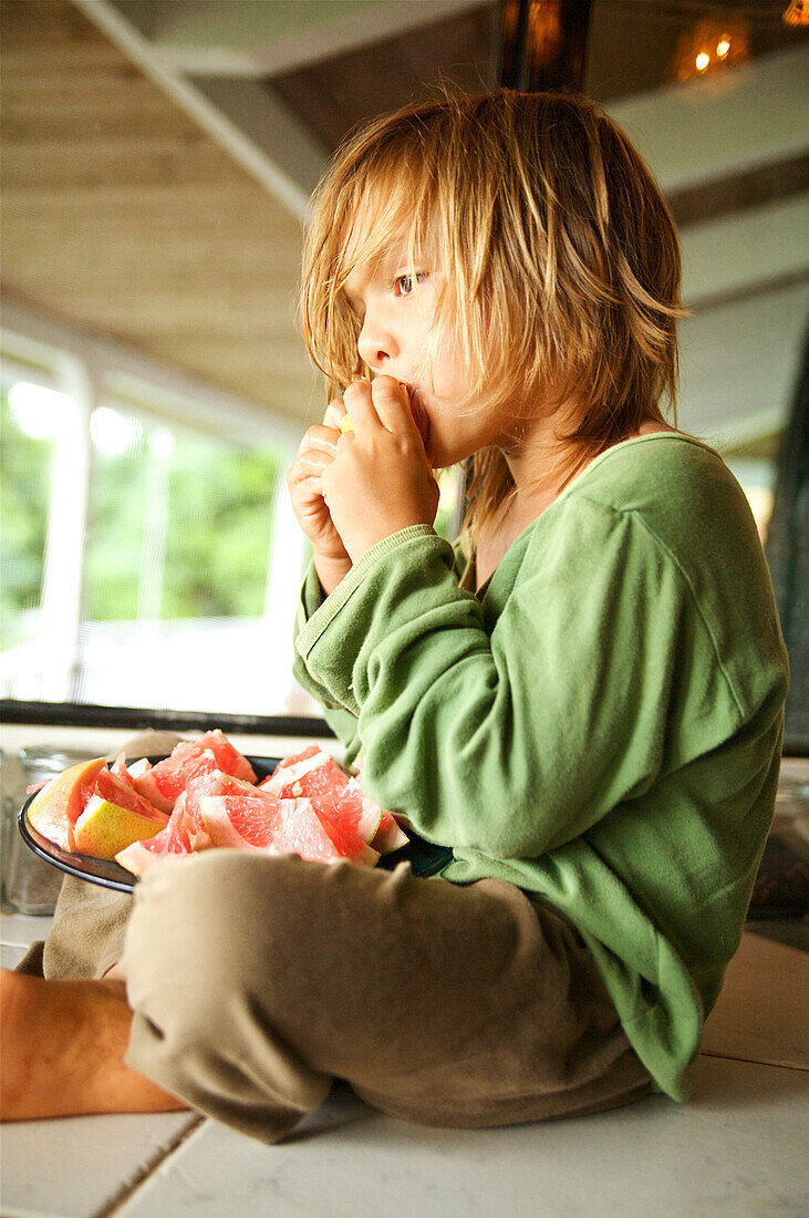 Hawaii, Kauai, Kilauea, Young boy sitting on porch eating grapefruit.
