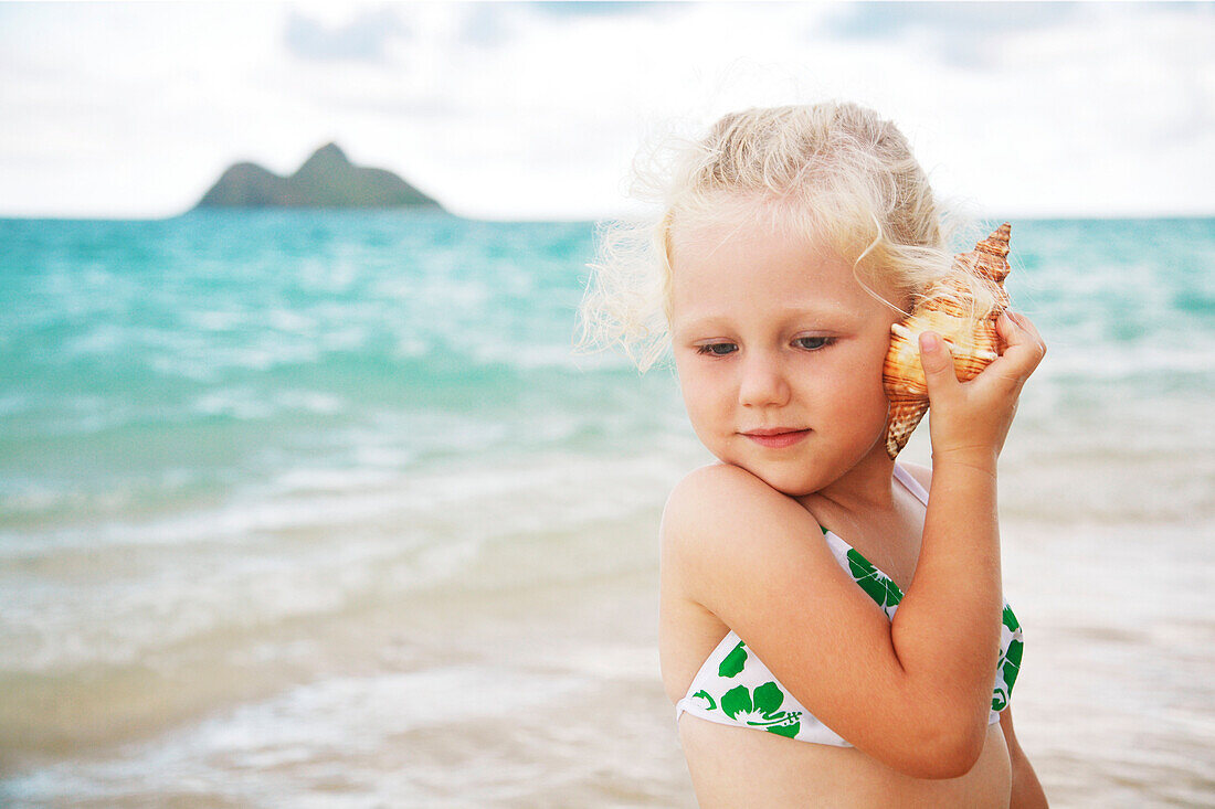 Hawaii, Oahu, Lanikai, Young girl listening to a shell.