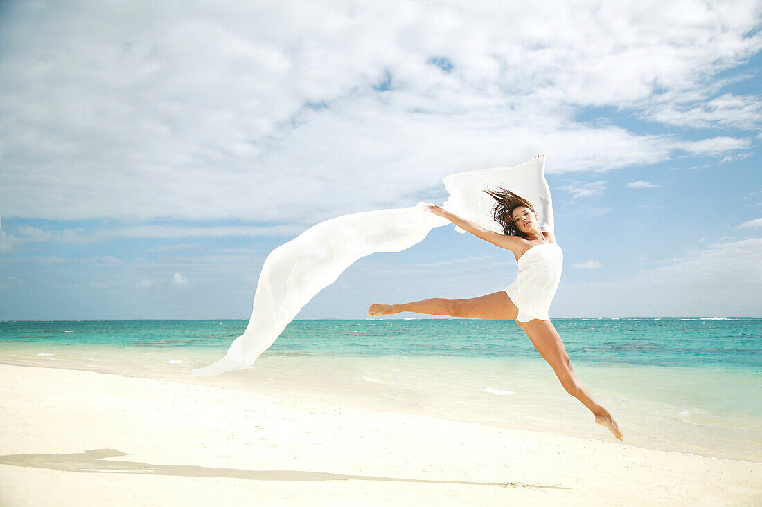 Hawaii, Oahu, Lanikai Beach, Beautiful female ballet dancer leaping into air on beach with white flowing fabric.