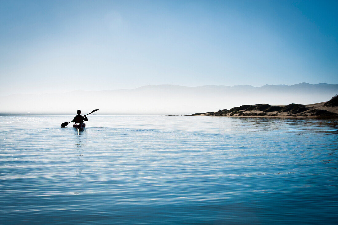 California, Morro Bay State Park, Woman kayaking in ocean, silhouette.