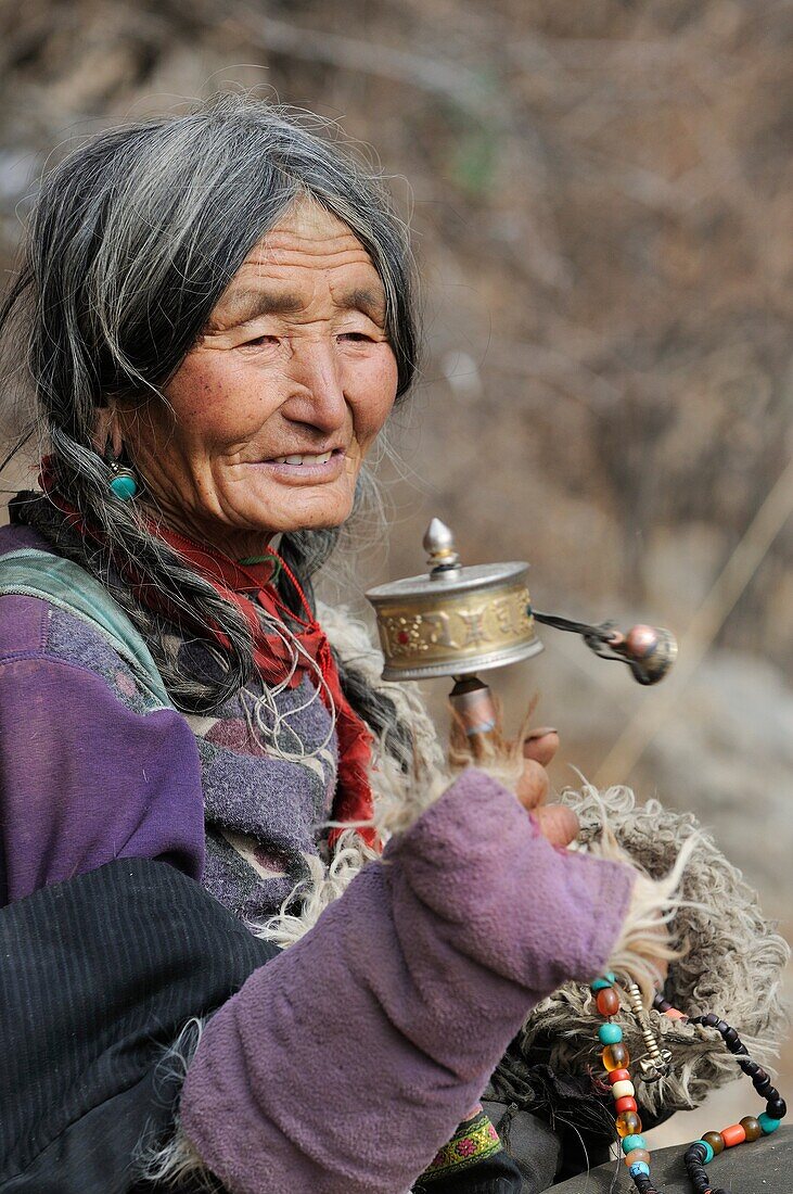 China, Gansu, Amdo, Xiahe county, Ganjia, Old tibetan woman spinning a prayer wheel