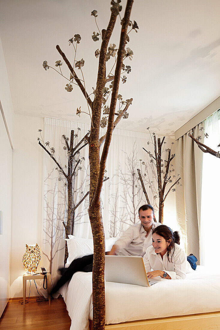 Young couple with laptop on a hotel bed, Milan, Lombardy, Italy