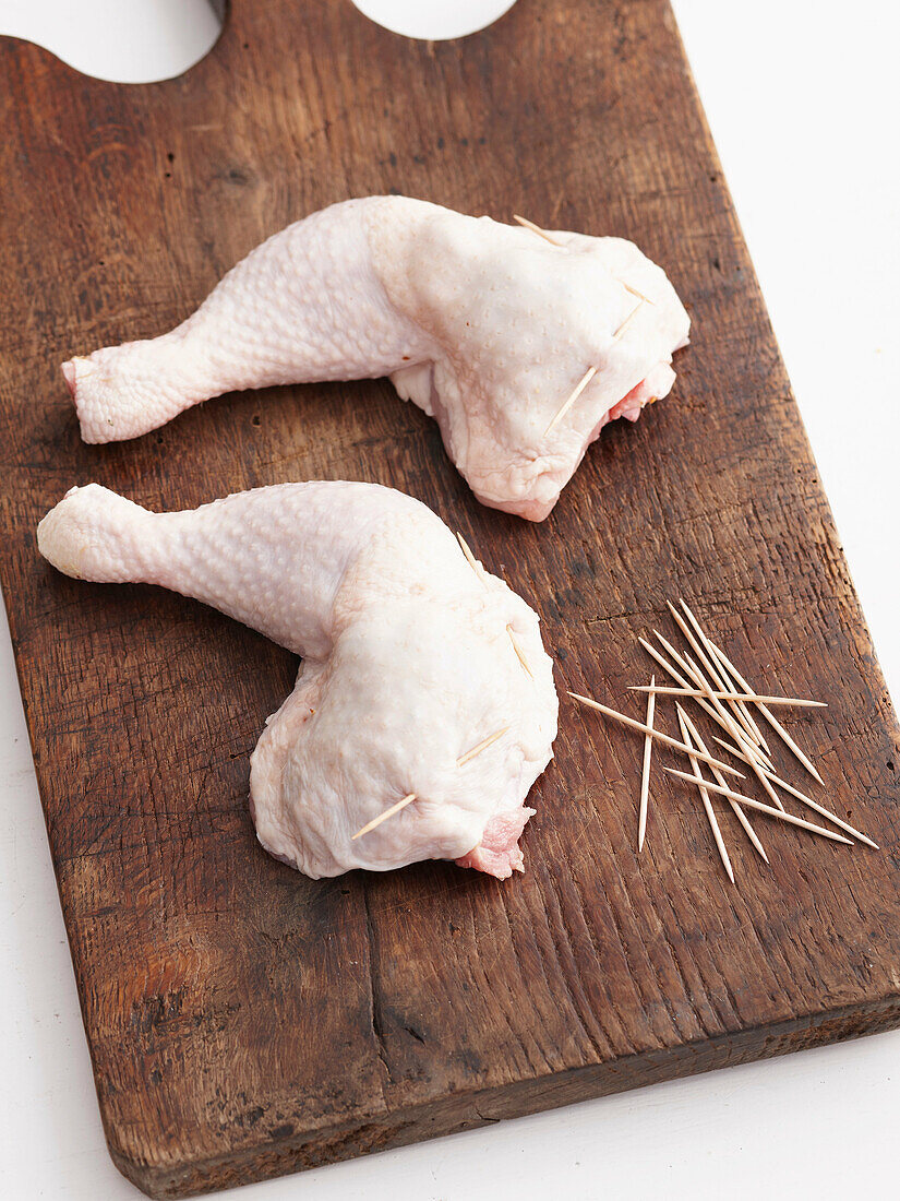 Raw chicken legs with toothpicks. Roast Chicken _ Pinning stuffed skin before cooking