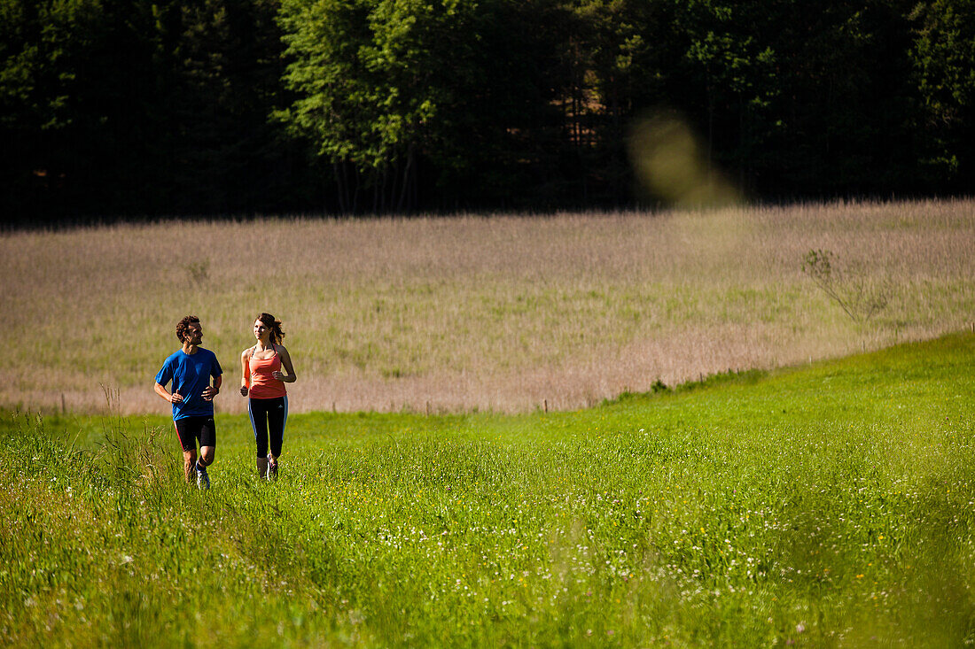 Two joggers running over a meadow, Upper Bavaria, Germany