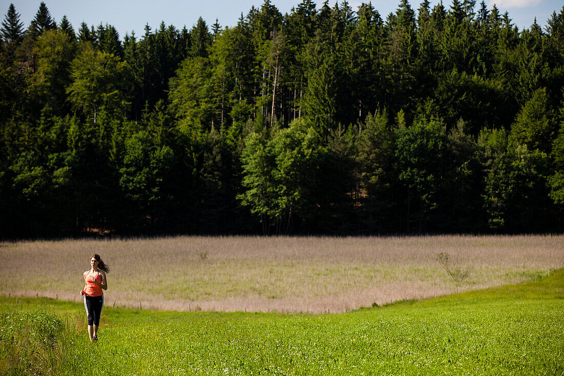 Junge Frau joggt über eine Wiese, Oberbayern, Deutschland