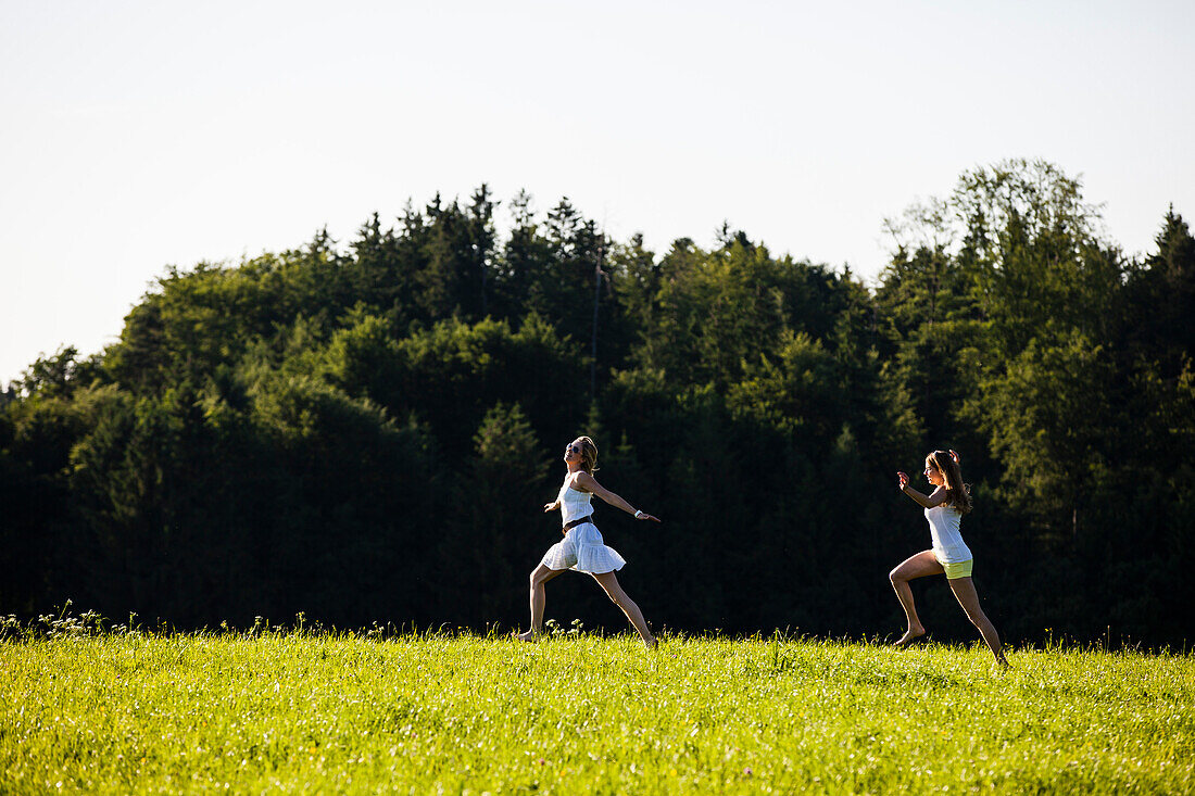 Two young woman running over a meadow, Upper Bavaria, Germany