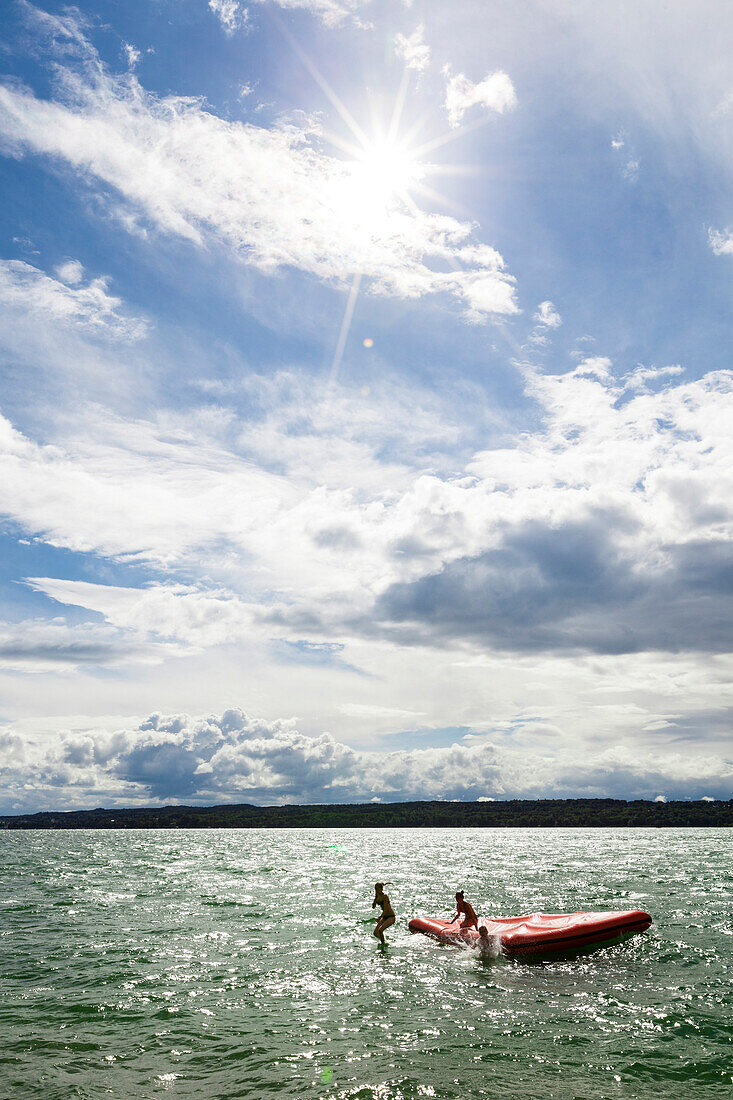 Three young women jumping from a floatable platform into Lake Starnberg, Bavaria, Germany