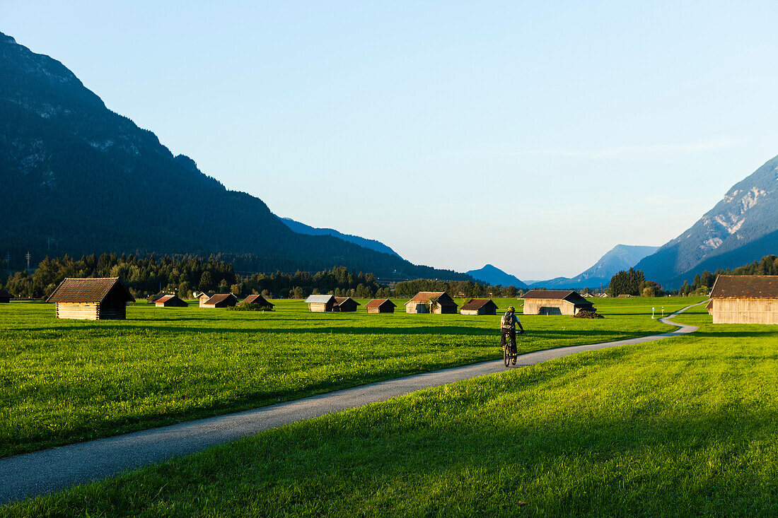 Mountainbiker fährt an Wiesen mit Heustadel vorbei, Grainau, Bayern, Deutschland