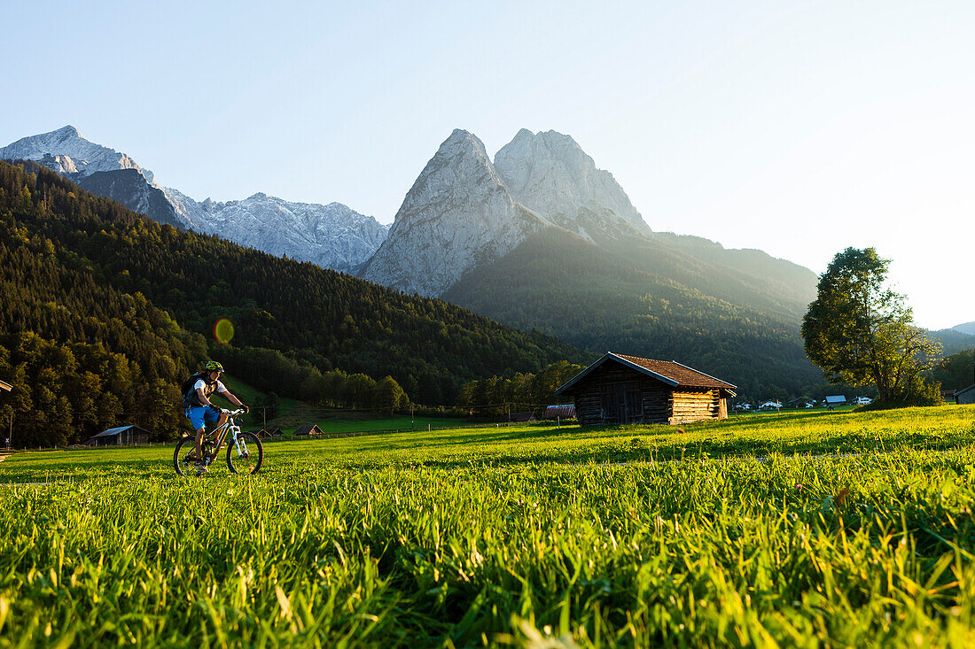 Mountainbiker fährt an Wiesen mit Heustadel vorbei, Grainau, Bayern, Deutschland