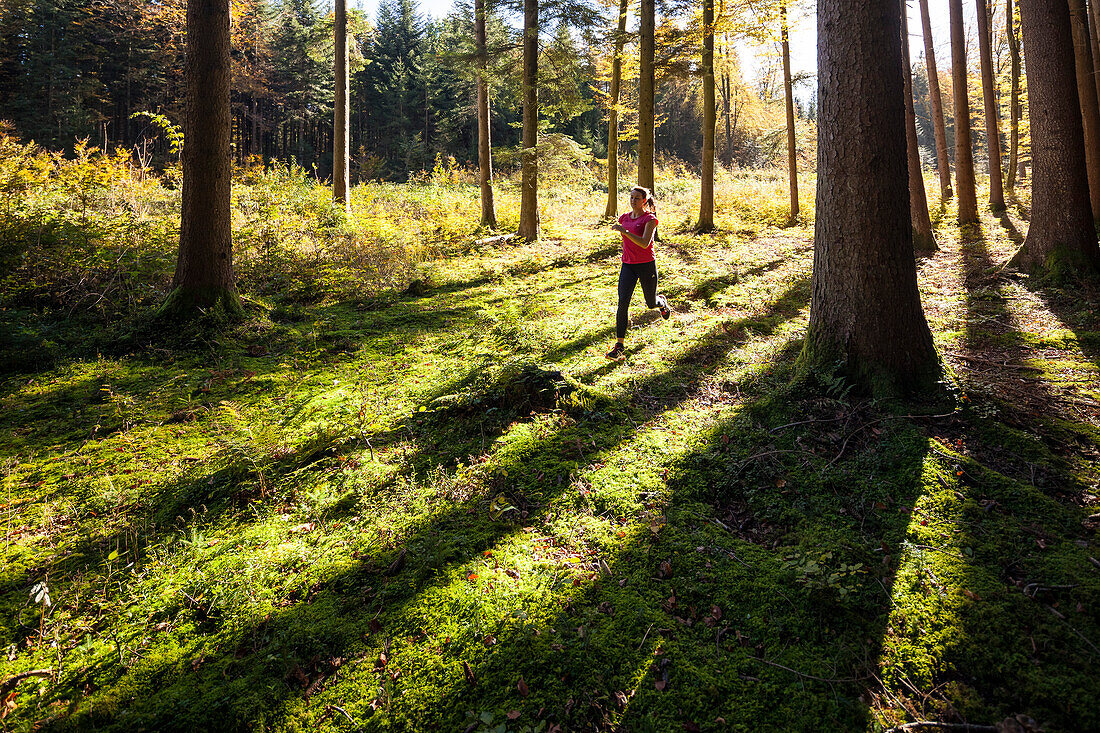 Junge Frau joggt durch herbstlichen Wald, Berg, Bayern, Deutschland