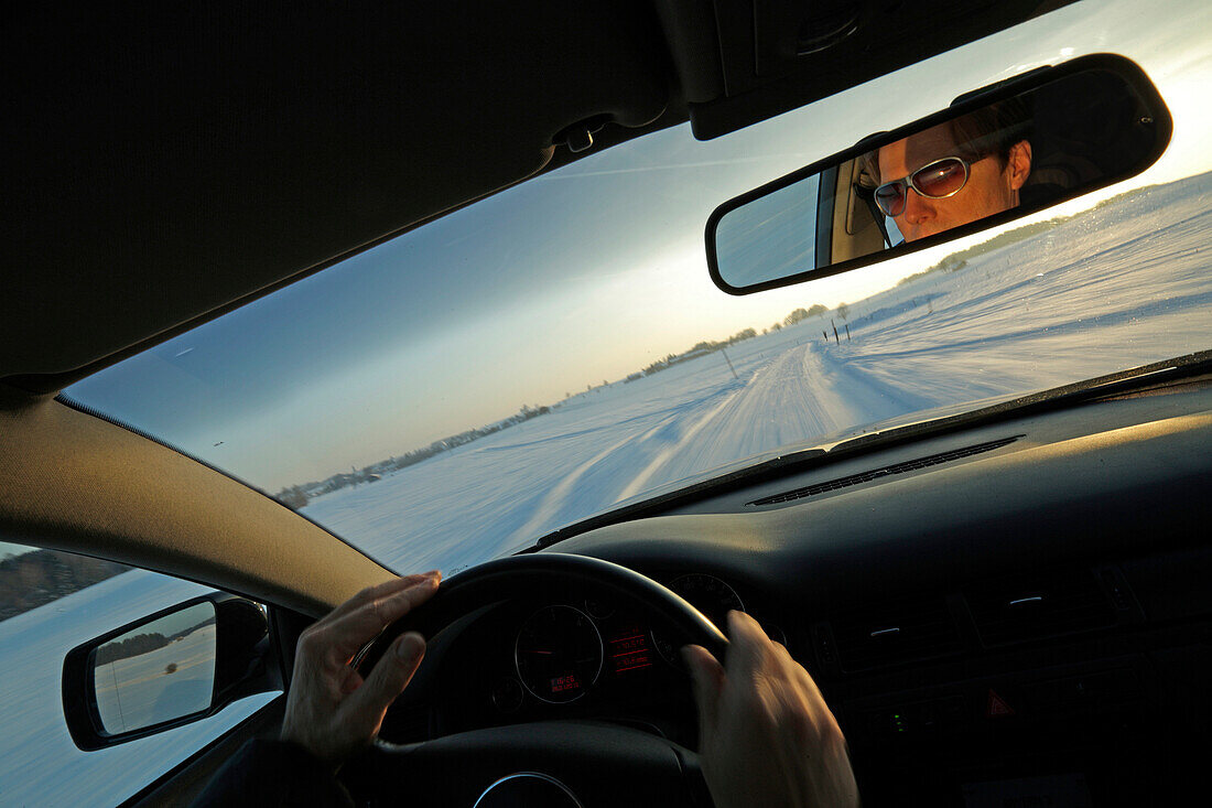 Man driving a car along a snow-covered street, Bavaria, Germany