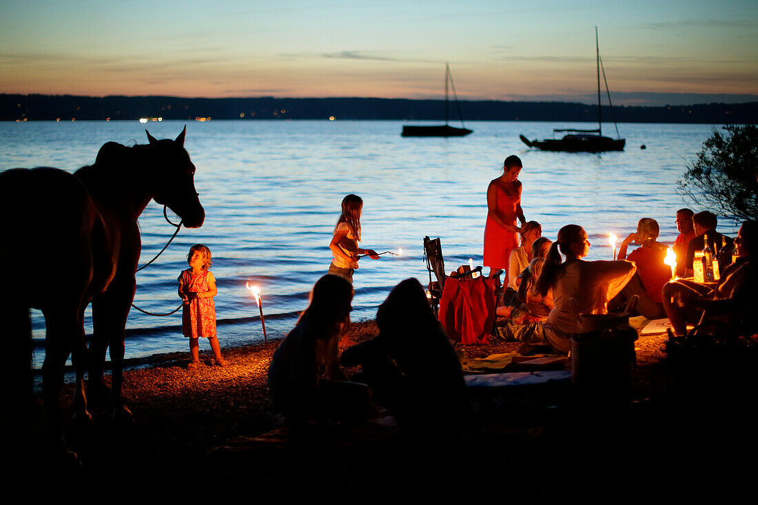 Adults and children with torches at lakeshore, lake Starnberg, Bavaria, Germany