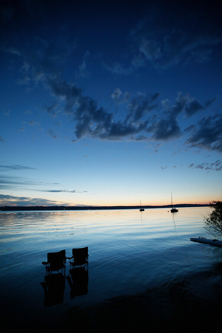 Zwei Klappstühle im Starnberger See in der Abenddämmerung, Bayern, Deutschland