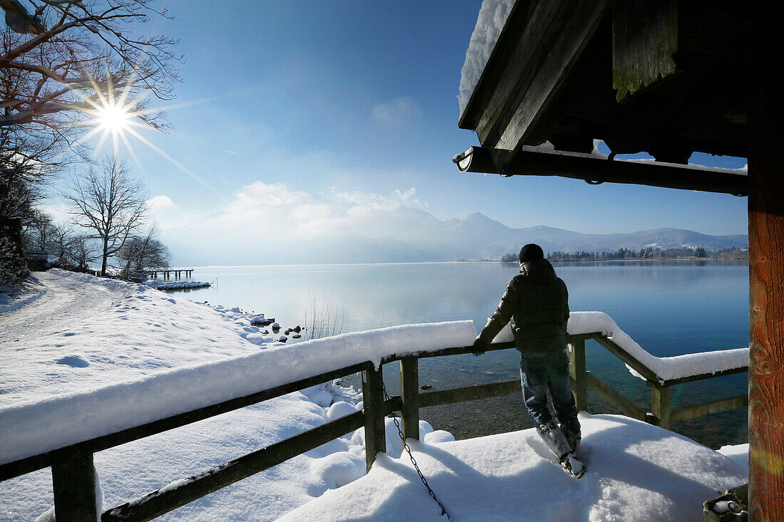Mann steht auf einem verschneitem Steg am Kochelsee, Oberbayern, Deutschland