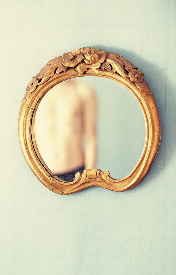 Shirtless adult male reflected in antique mirror hanging on wall