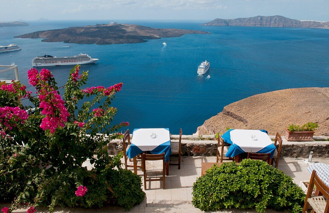 Looking down at restaurant with romantic tables and the sea with ships at harbor with statue in Santorini Greece in Greek Islands