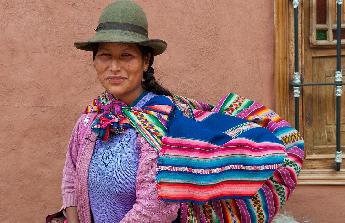 Traditional woman in dress and hat with baby on back in small town of Pisaq Peru