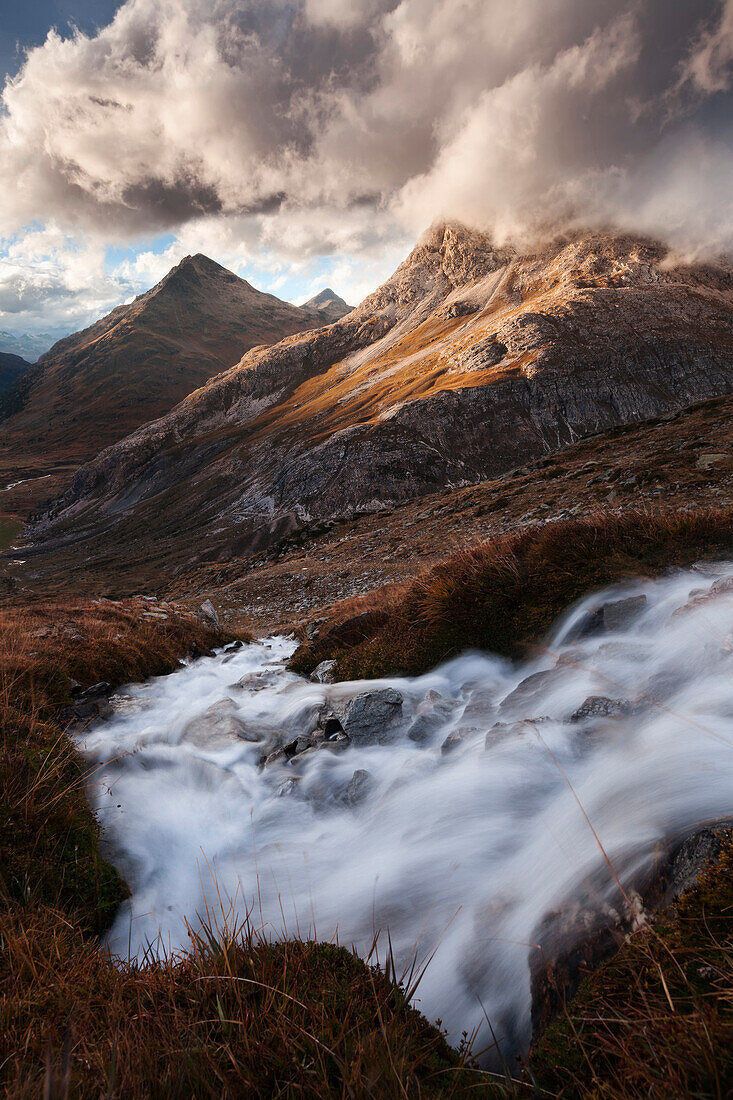 Dramatic play of light over a mountain torrent above the Bernina valley with the summits of Piz Albris (3137 m) and Piz Alo (2975 m) in the background, Engadin, Switzerland