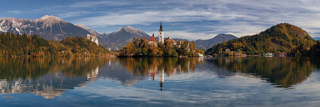 Picturesque view of St. Mary's Church and its reflection in the Lake Bled in autumn, in the background the castle of Bled soars in front of the Julian Alps, Gorenjska, Slovenia