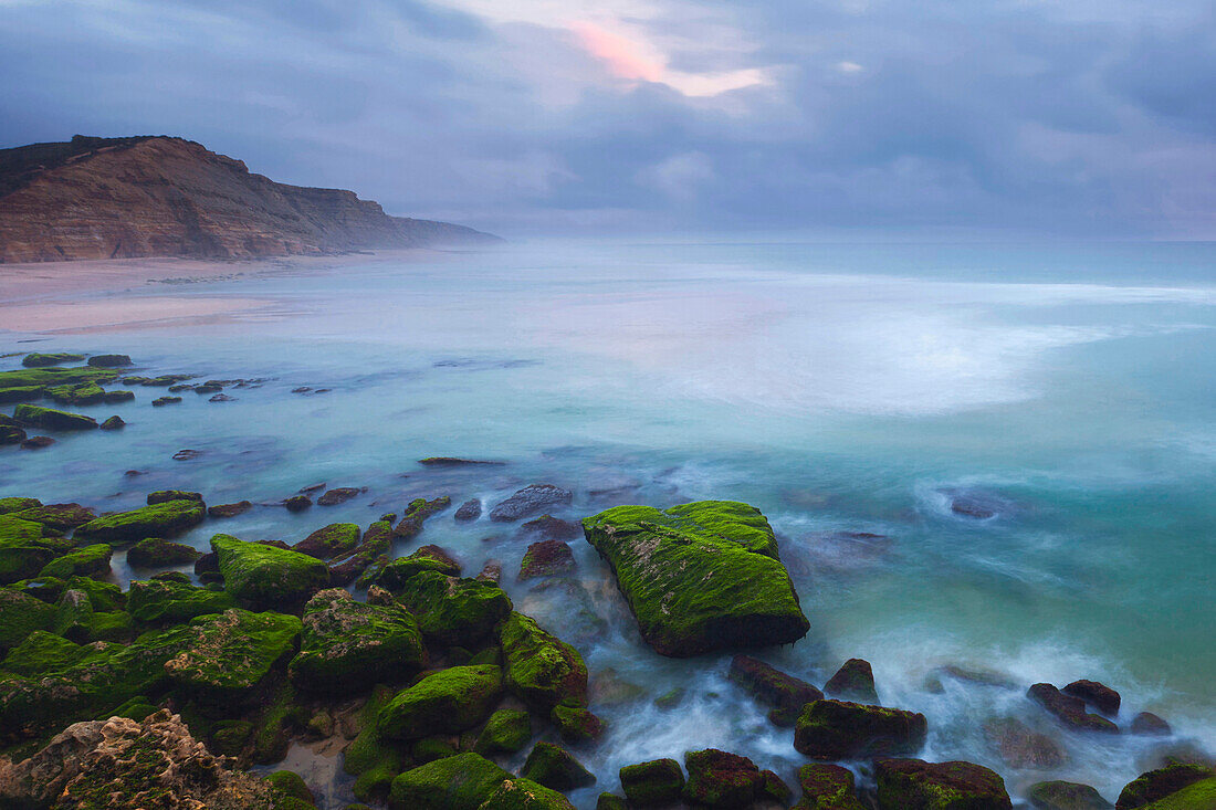 Turquoise blue water and moss-covered sandstone rocks on the beach Foz de Lizandro in the Sintra-Cascais National Park, Ericeira, Portugal