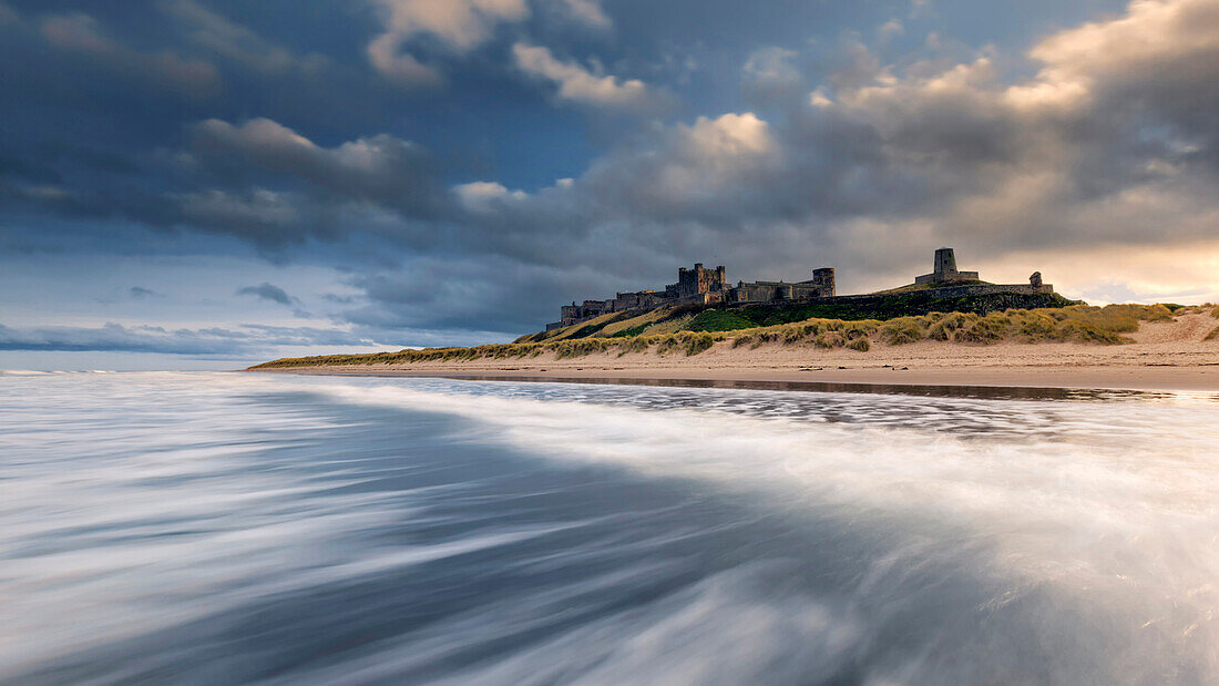 Incoming surf with the view to the impressive Bamburgh Castle in Northumberland, England, United Kingdom