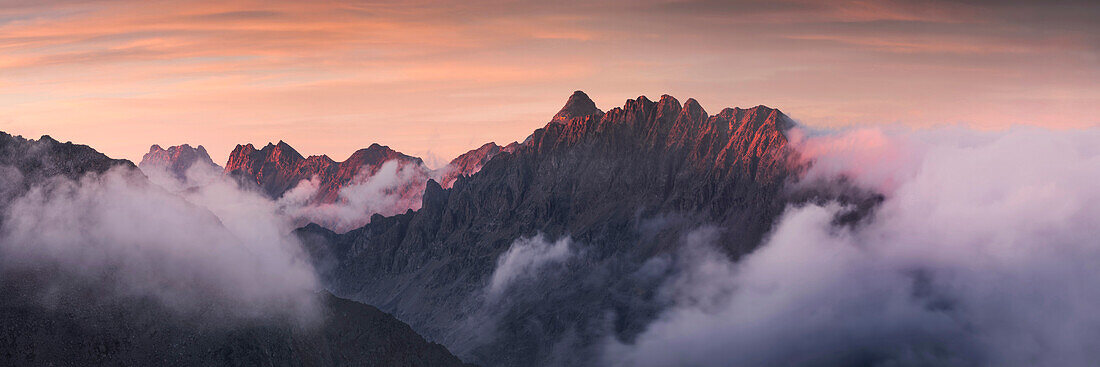 Blick über das nebelverhangenen Berninatal auf die erleuchteten Gipfel Piz Languard und Piz Muragl links und Piz Albris rechts, Engadin, Schweiz