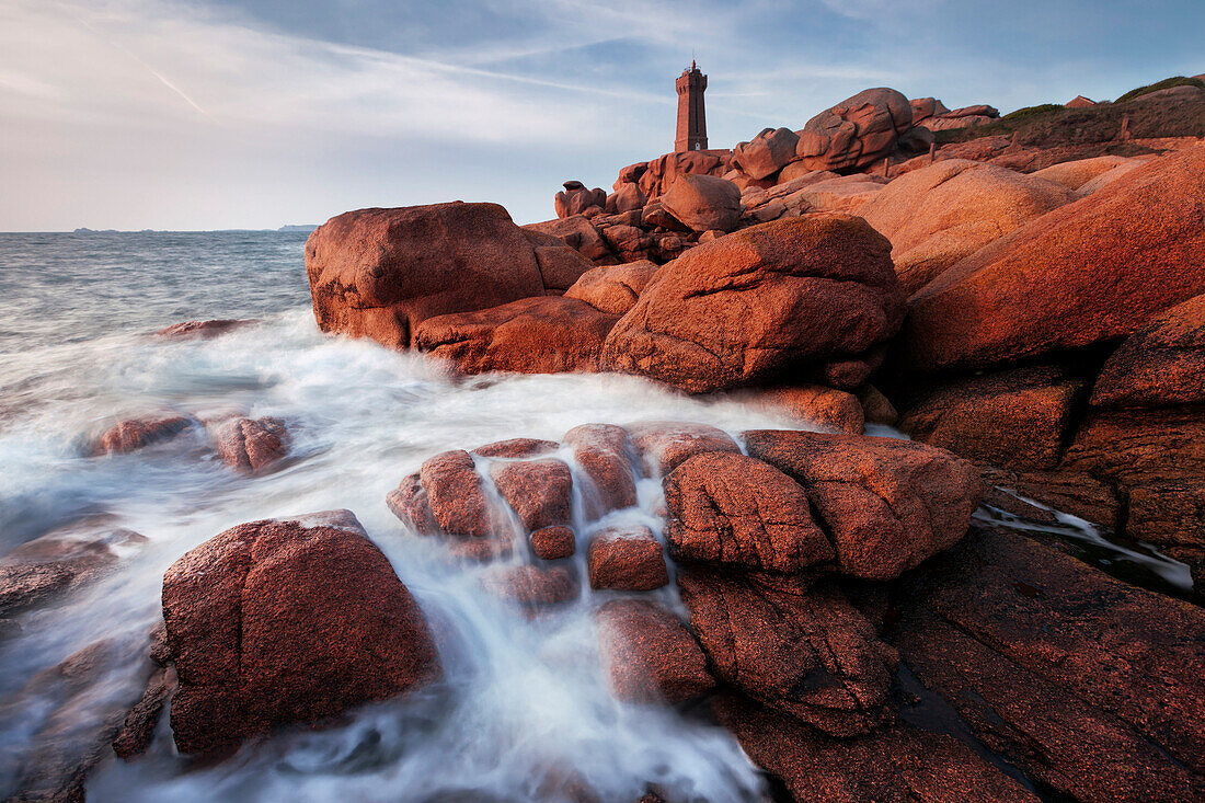 Der Leuchtturm Mean Ruz mit den roten Felsen der Côte de Granit Rose in der Morgensonne, Bretagne, Frankreich