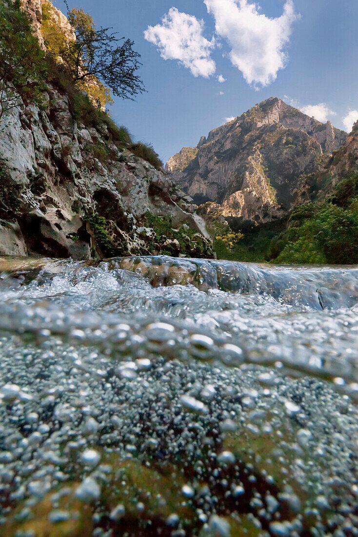 View beneath the water surface of the mountain stream Rio Deva in the evening light with mountains of the Picos de Europa National Park in the background, Cantabria, Spain