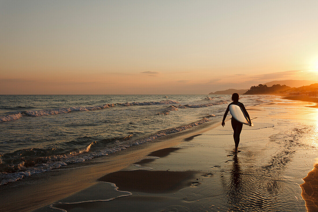 Surfer läuft den Strand entlang bei Sonnenuntergang, Castiglione della Pescaia, Mittelmeer, Provinz Grosseto, Toskana, Italien, Europa