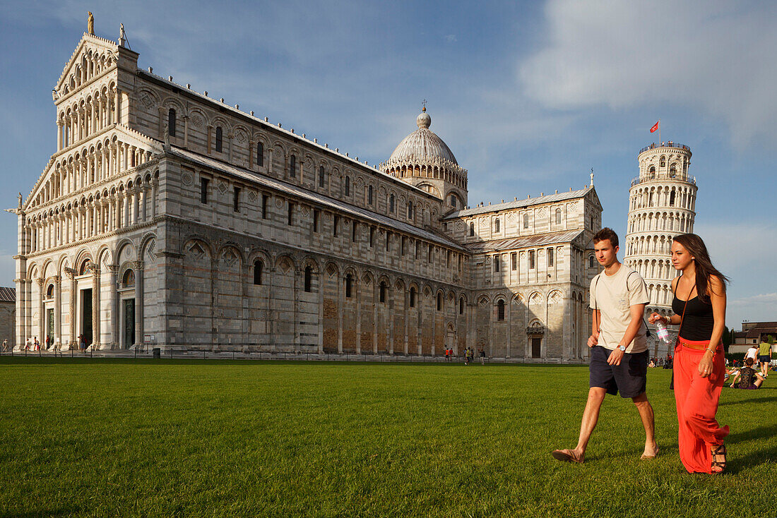 Couple walking across the grass infront of the Duomo, cathedral, campanile, bell tower, Torre pendente, leaning tower, Piazza dei Miracoli, square of miracles, Piazza del Duomo, Cathedral Square, UNESCO World Heritage Site, Pisa, Tuscany, Italy, Europe